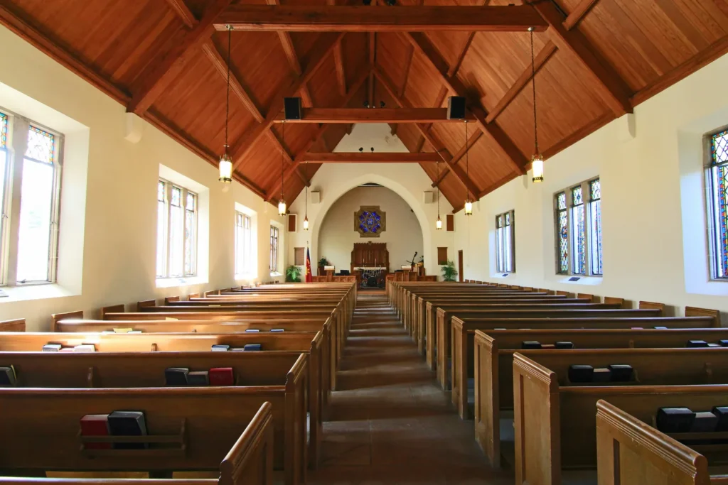 Sunlit church interior with a wooden ceiling and empty pews