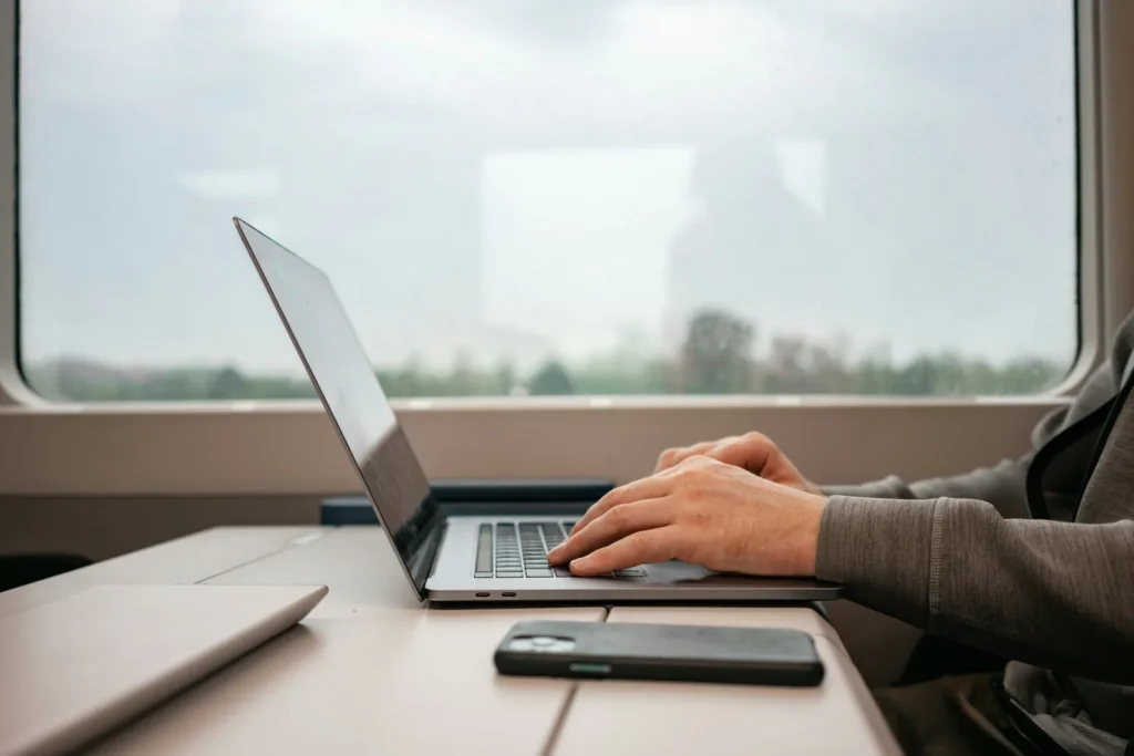 Hands typing on a laptop beside a large window