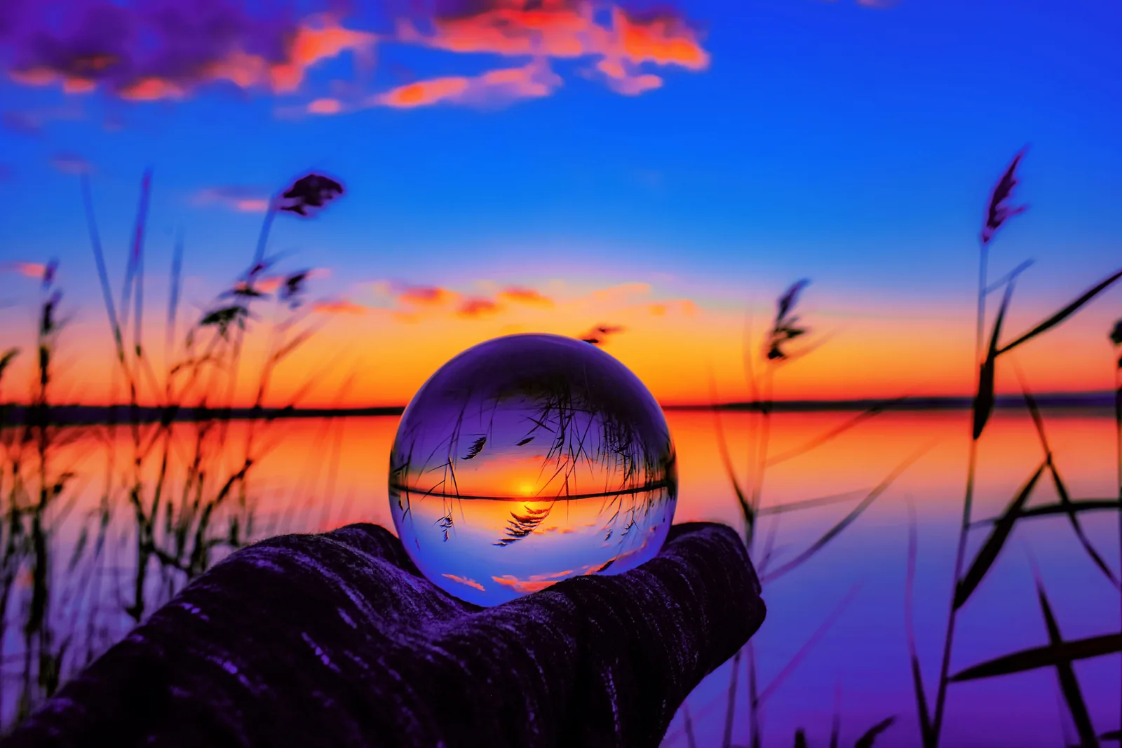 Glass sphere held against a sunset over the water
