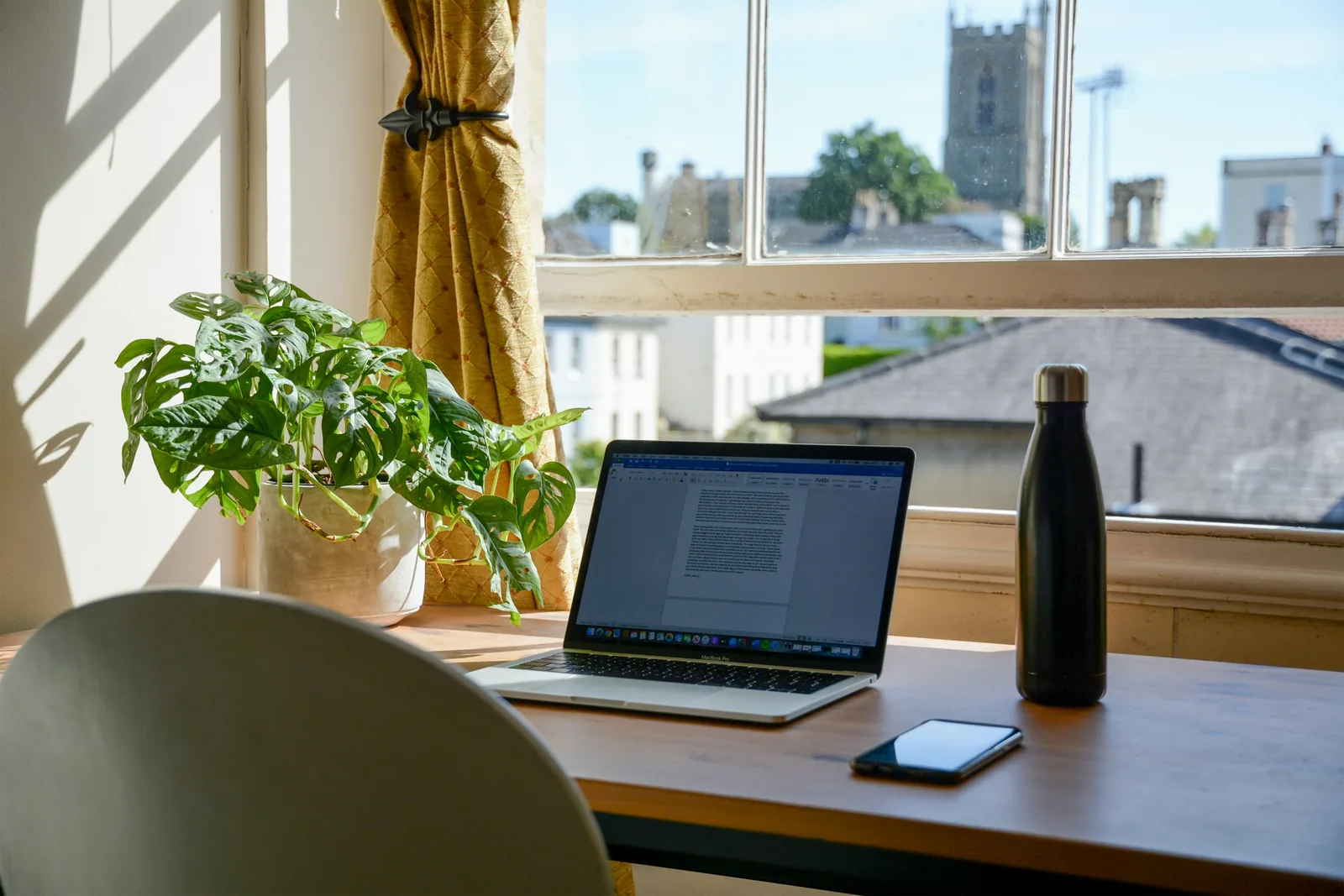 Laptop on a desk by a sunny window with a church tower outside