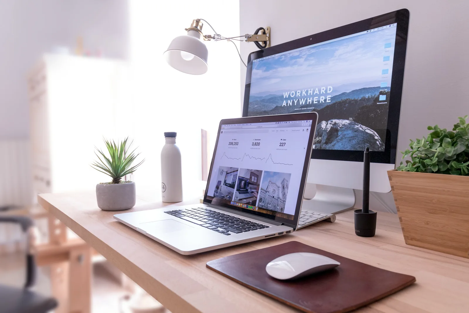 Desk with a laptop and a monitor showing a website in daylight